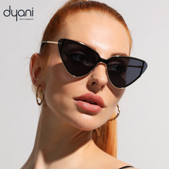 Woman wearing Dyani cat-eye sunglasses with gold frame and dark lenses, striking pose on white background, exuding fierce elegance.