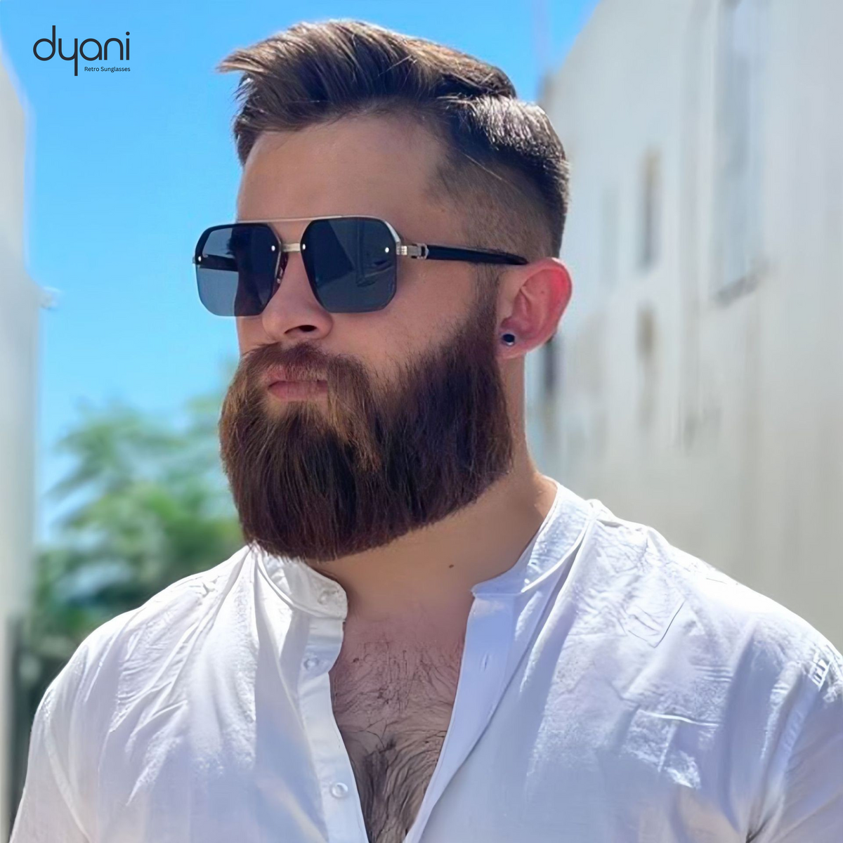 Man wearing Dyani The Apex sunglasses with sleek boxy design, standing outdoors in white shirt, stylish summer fashion accessory.