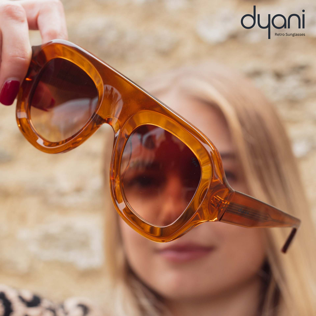 Woman holding Velora bold rounded acetate sunglasses with gradient UV400 lenses.