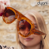 Woman holding Velora bold rounded acetate sunglasses with gradient UV400 lenses.