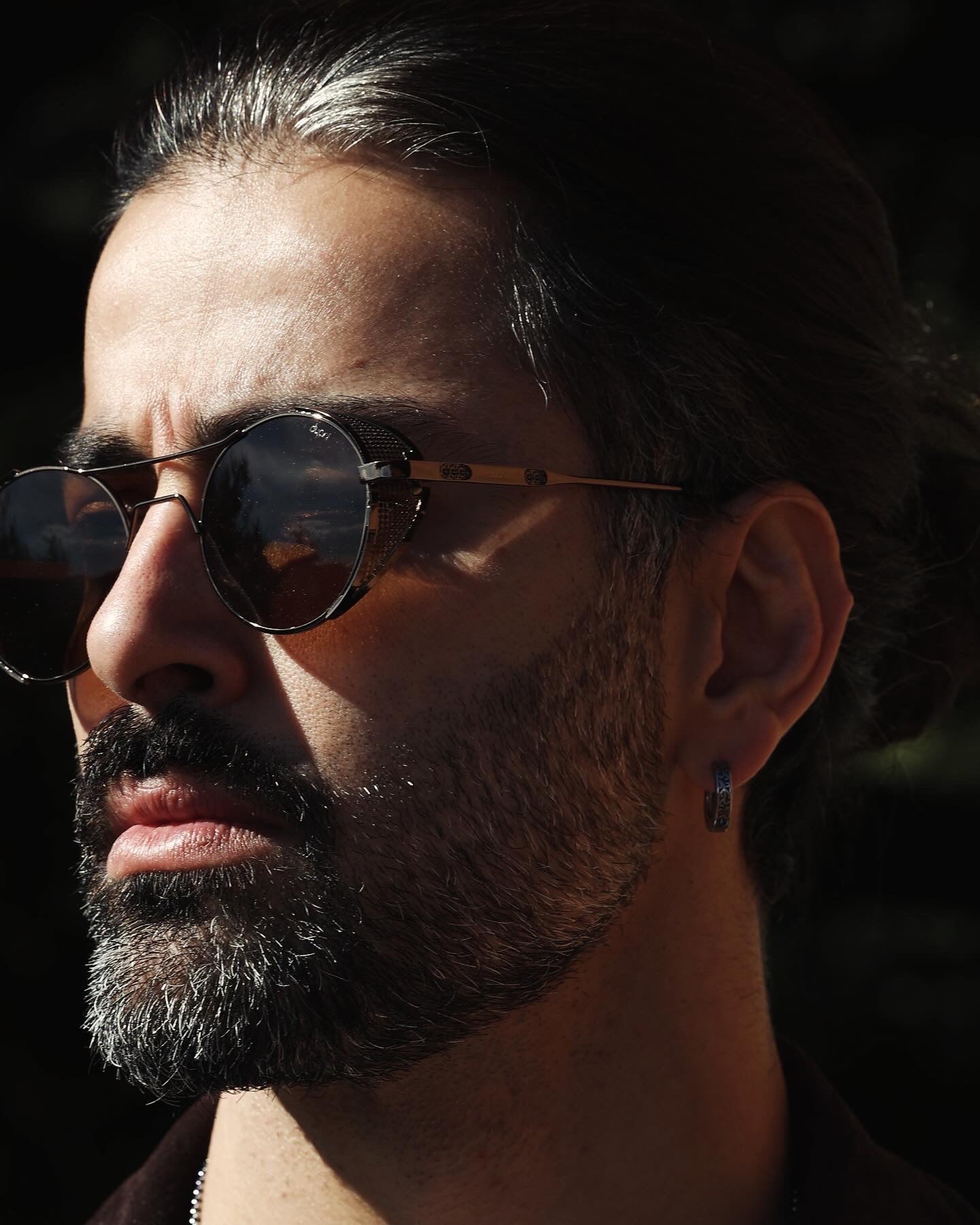 Man wearing Dyani Dusk Seeker sunglasses with vintage-modern design, black lenses, and white temples in sunlight.