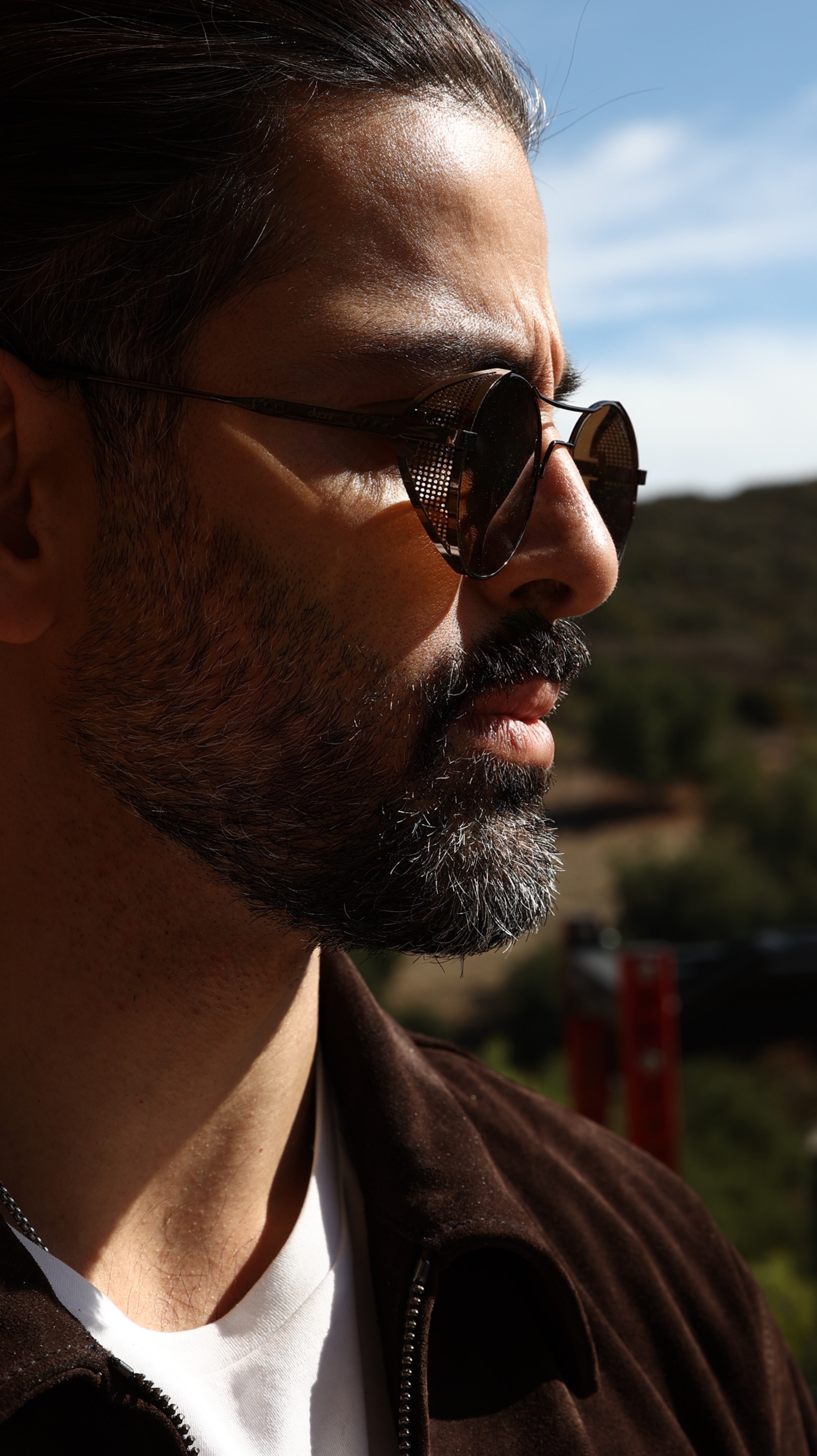 Man wearing Dyani Dusk Seeker Mesh Edge sunglasses with metal frame, modern design, and UV 400 black lenses outdoors.